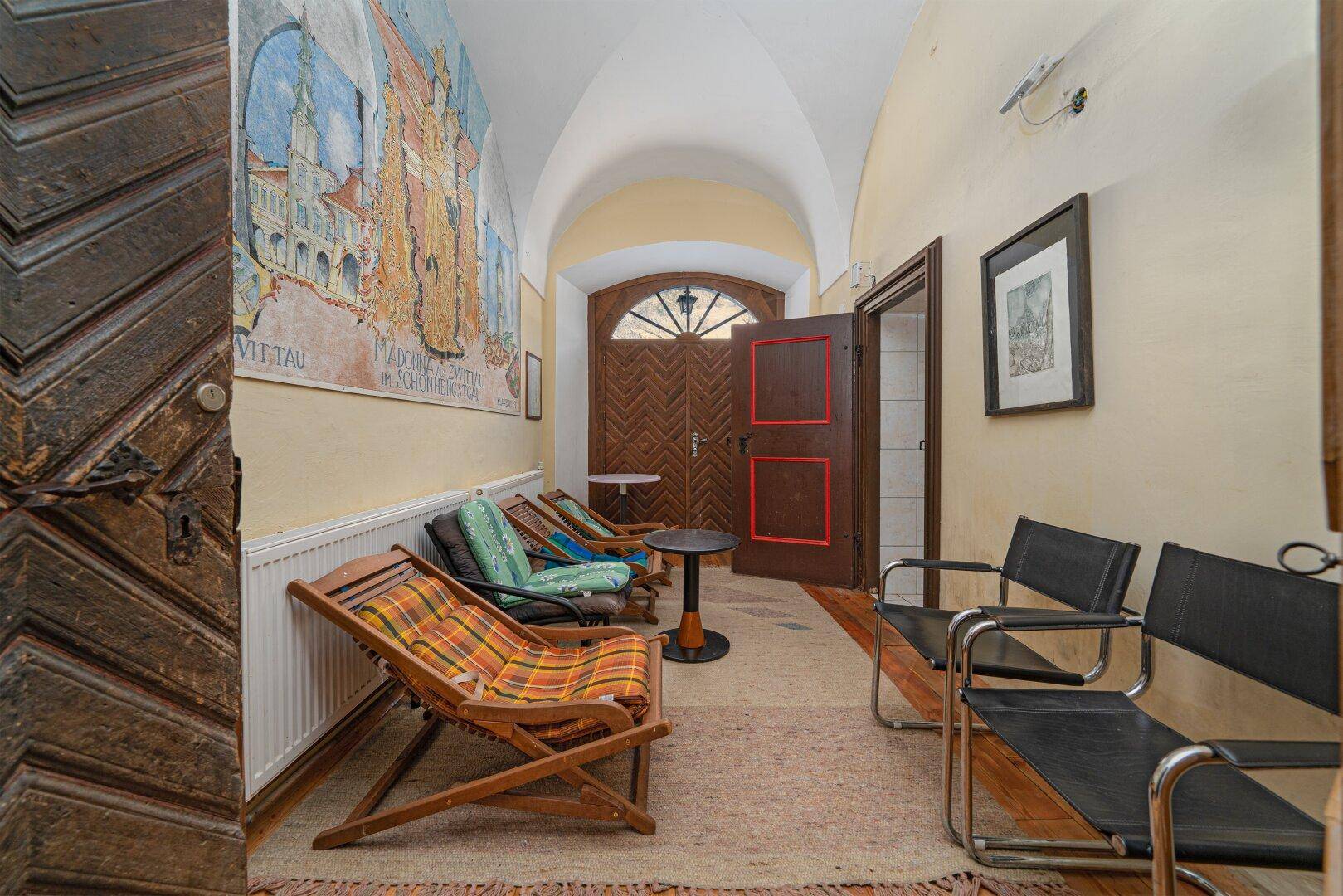 Historischer Eingangsbereich mit Gewölbedecke, Holztür und traditionellen Sitzgelegenheiten.