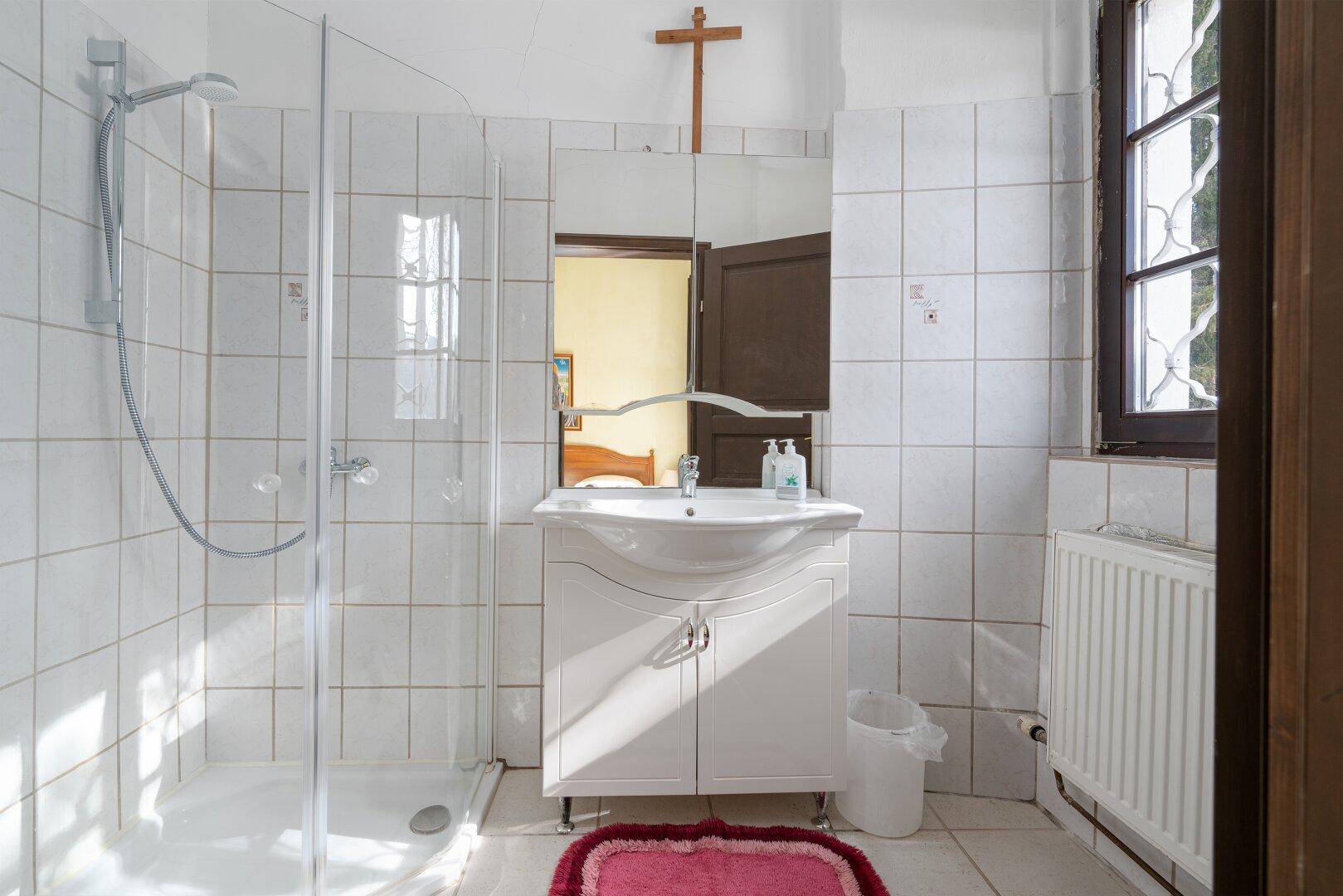 Badezimmer mit weißen Fliesen, Dusche und Fenster, bietet ausreichend Tageslicht.