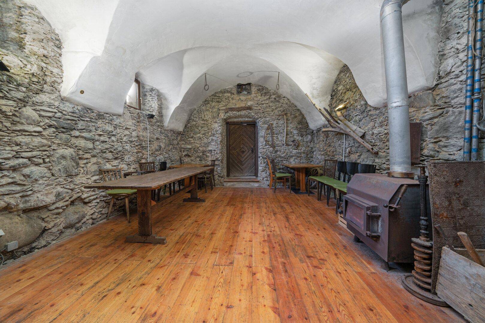 Rustikaler Kellerraum mit Steingewölbe, Holzdielenboden und einem großen Holzofen.