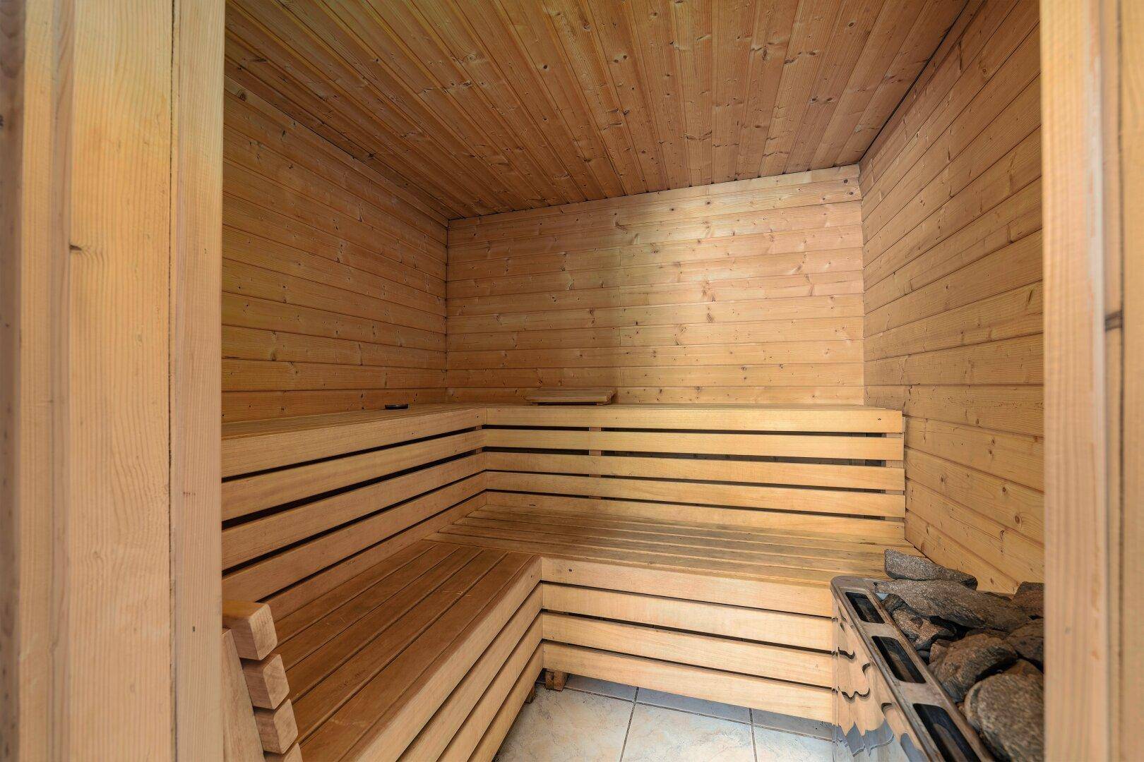 Innenansicht einer traditionellen Holzsauna mit mehreren Sitzebenen und Heizofen.