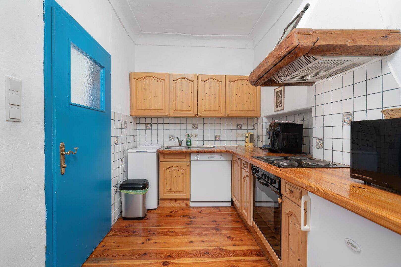 Funktionale Küche mit Holzdielenboden, Holzschränken und blauer Tür, hell und einladend.