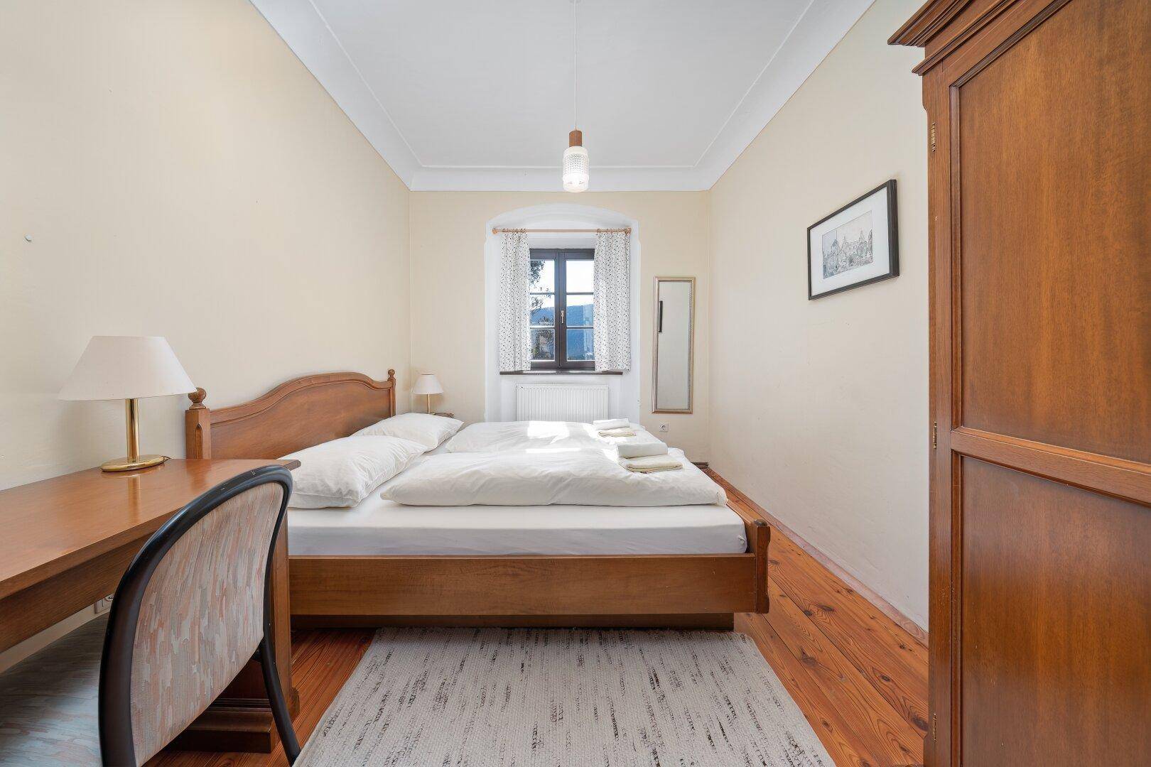 Schlafzimmer mit Holzdielenboden, Schreibtisch und traditionellem Kleiderschrank, funktional eingerichtet.