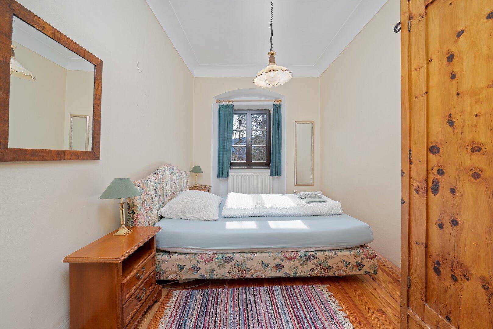 Schlafzimmer mit Holzdielenboden, traditionellem Bett und Kleiderschrank, gemütlich und hell.