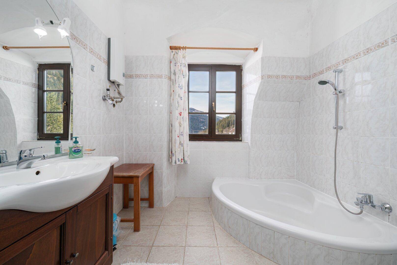 Badezimmer mit weißen Fliesen, Badewanne und Fenster, bietet einen Blick ins Grüne.