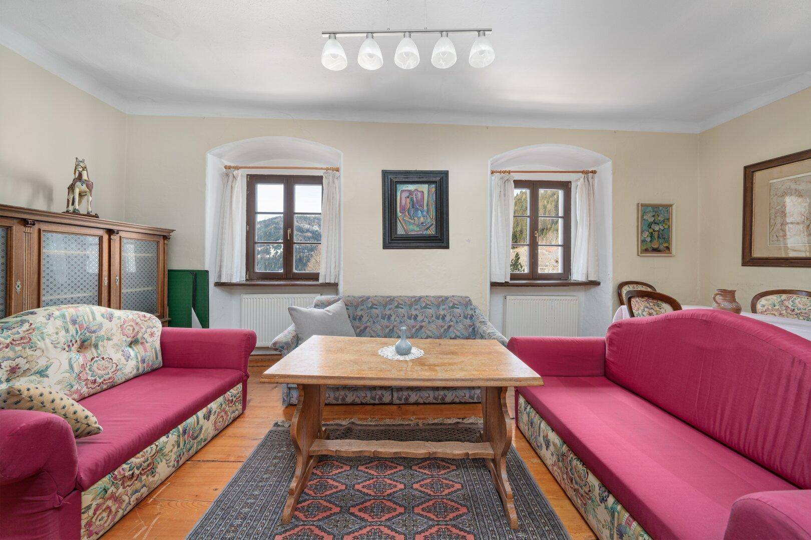 Wohnzimmer mit Holzdielenboden, bequemen Sofas und traditionellem Teppich, hell und einladend.