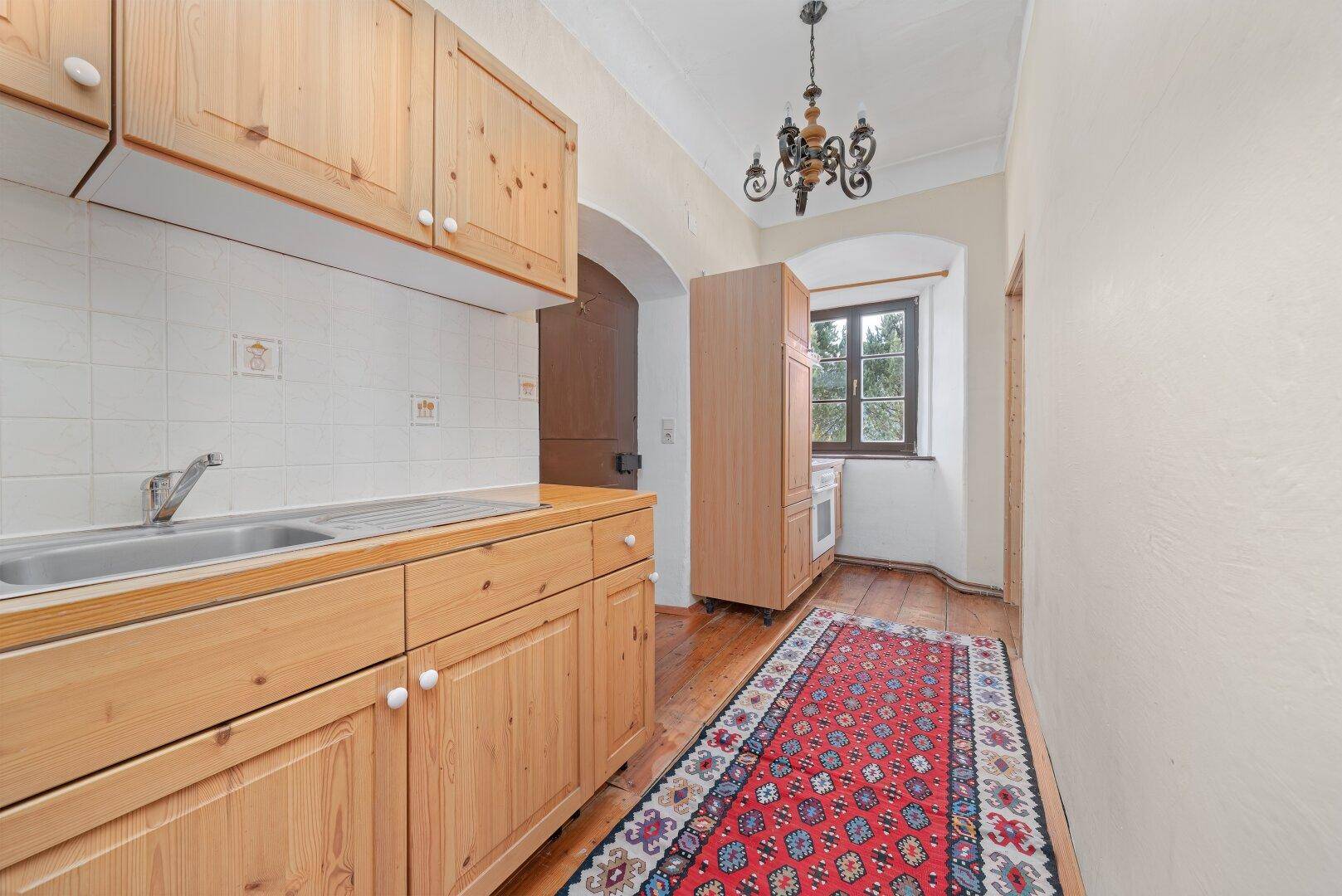 Kleine Küche mit Holzdielenboden, Holzschränken und traditionellem Teppich, funktional eingerichtet.