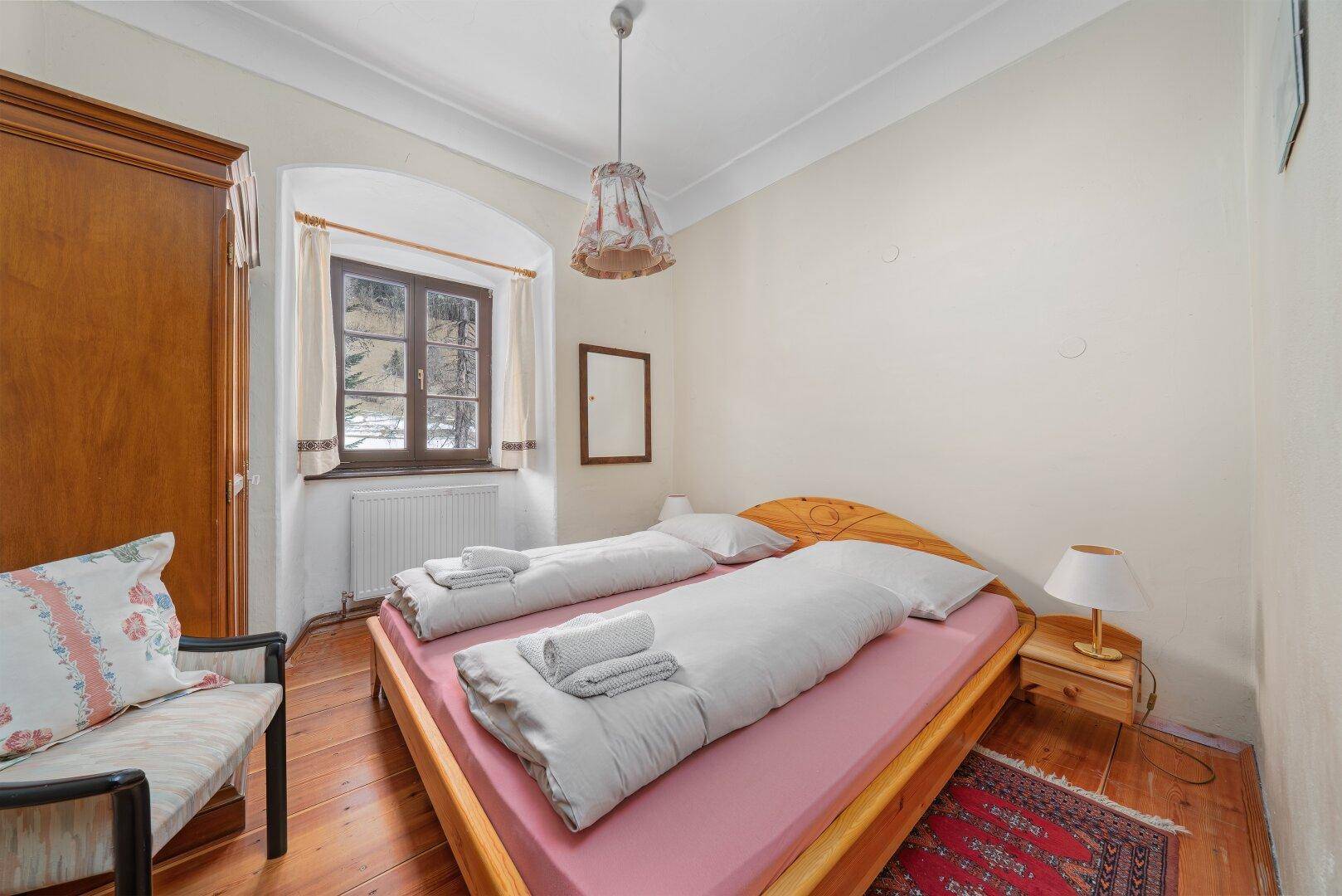 Schlafzimmer mit Holzdielenboden, traditionellen Möbeln und Blick auf die verschneite Landschaft.