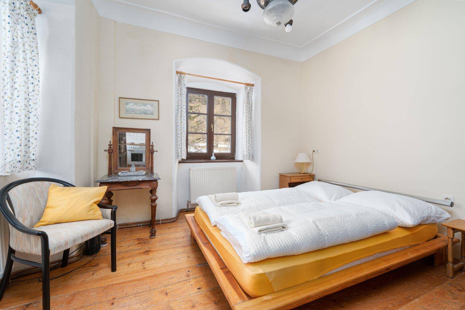 Schlafzimmer mit Holzdielenboden, traditionellen Möbeln und Blick auf die verschneite Landschaft.