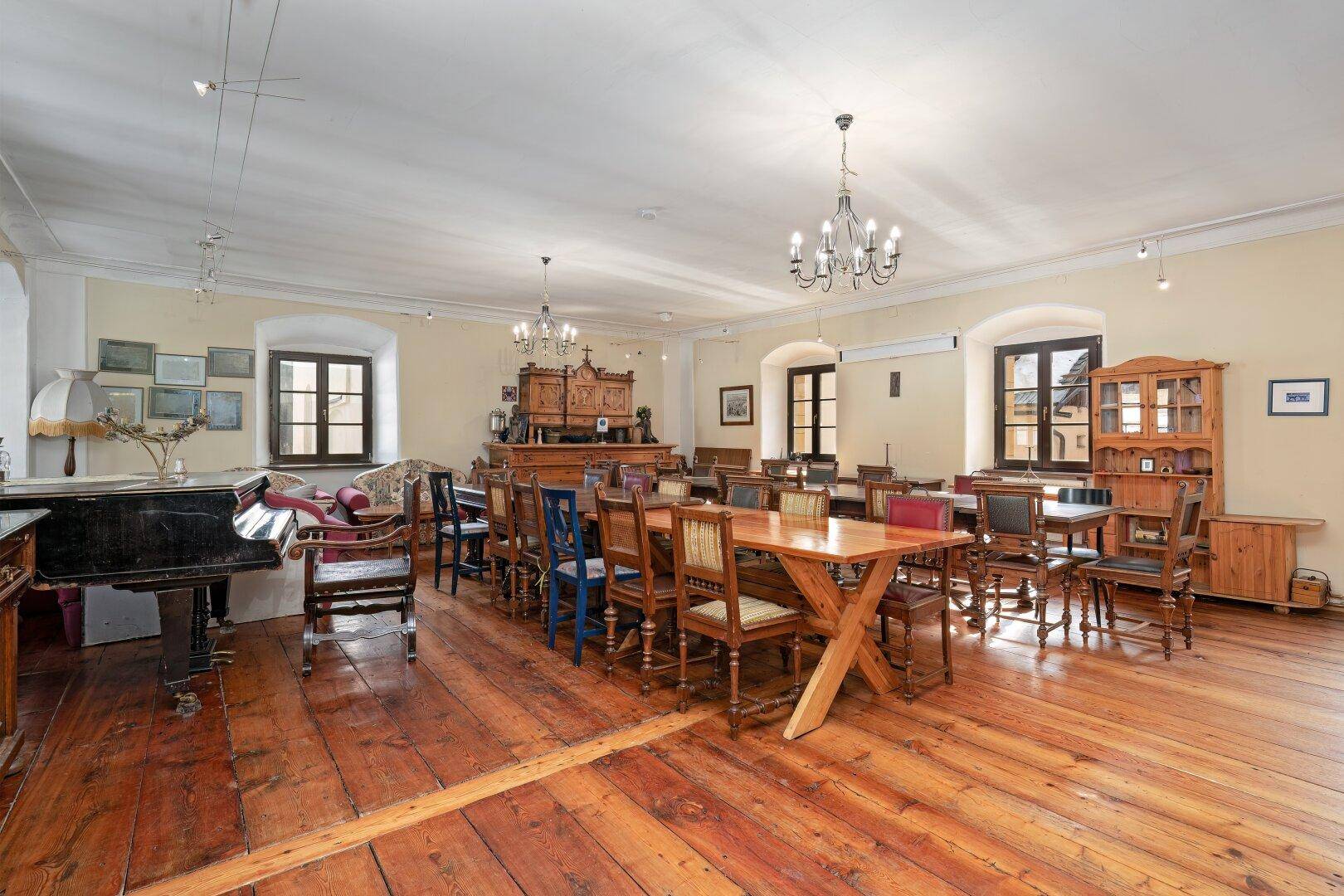Großer Speisesaal mit Holzdielenboden, mehreren Esstischen und Kronleuchtern, ideal für Veranstaltungen.