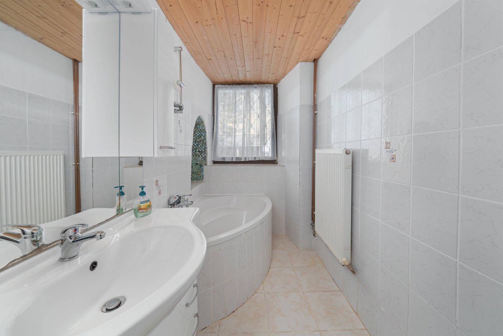 Badezimmer mit weißen Fliesen, Badewanne und Holzdecke, hell und funktional.