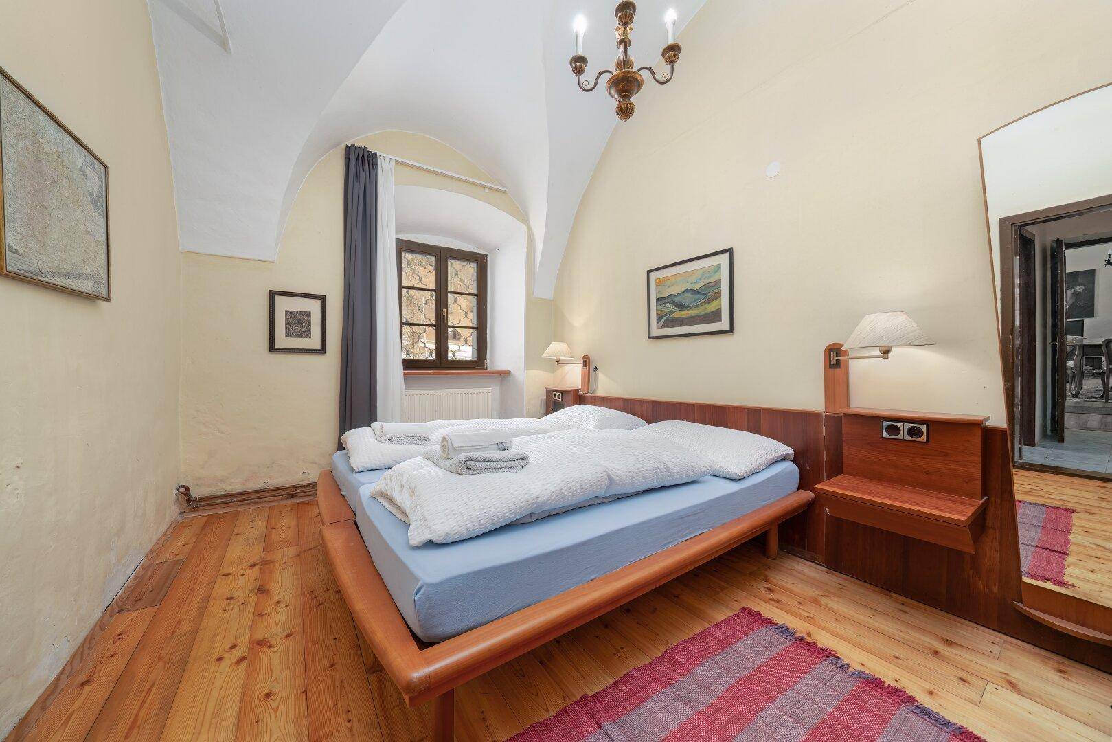 Schlafzimmer mit Holzdielenboden, Gewölbedecke und großem Spiegel, hell und geräumig.