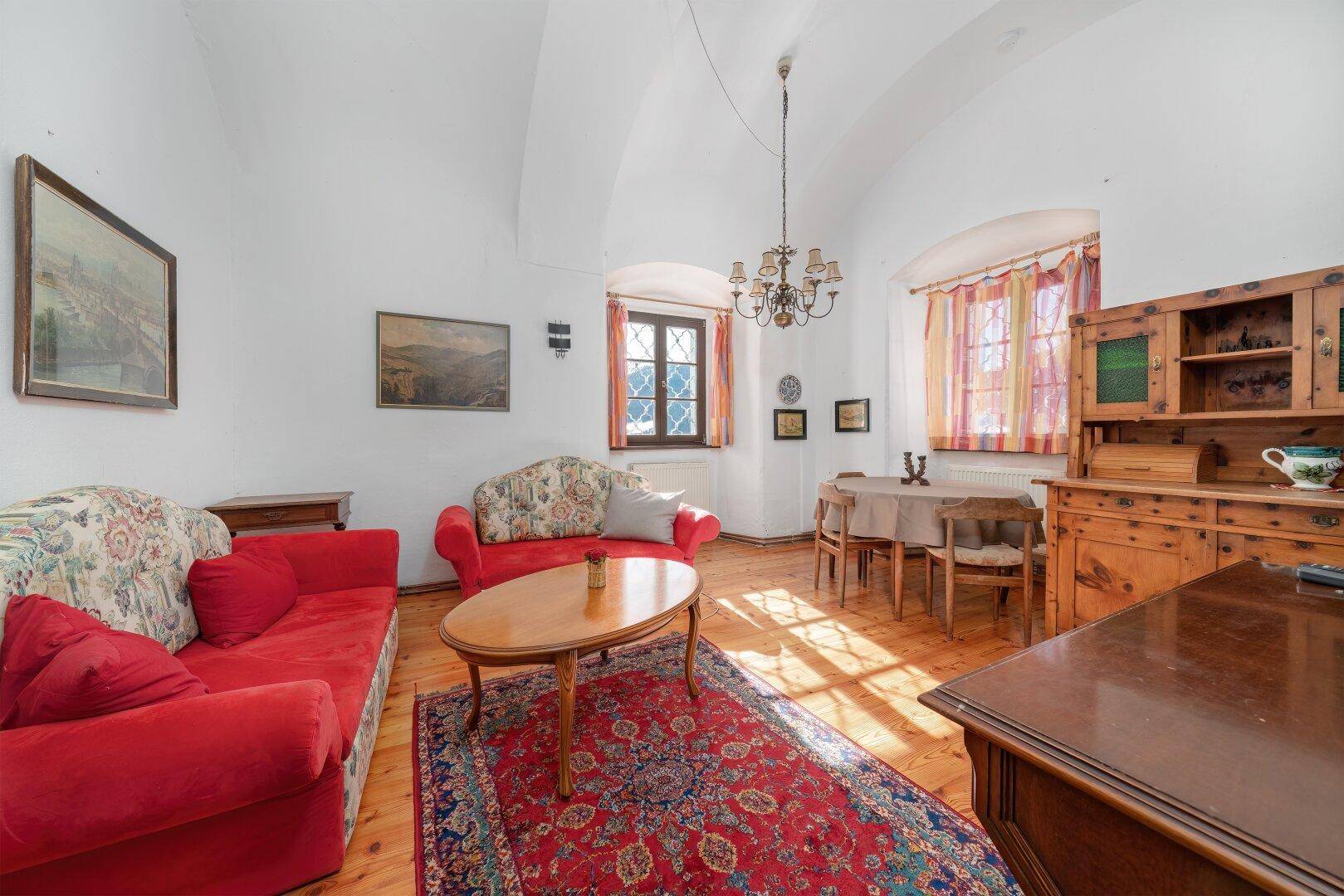 Gemütlicher Wohn- und Essbereich mit Holzdielenboden, roten Sofas und traditionellem Teppich.