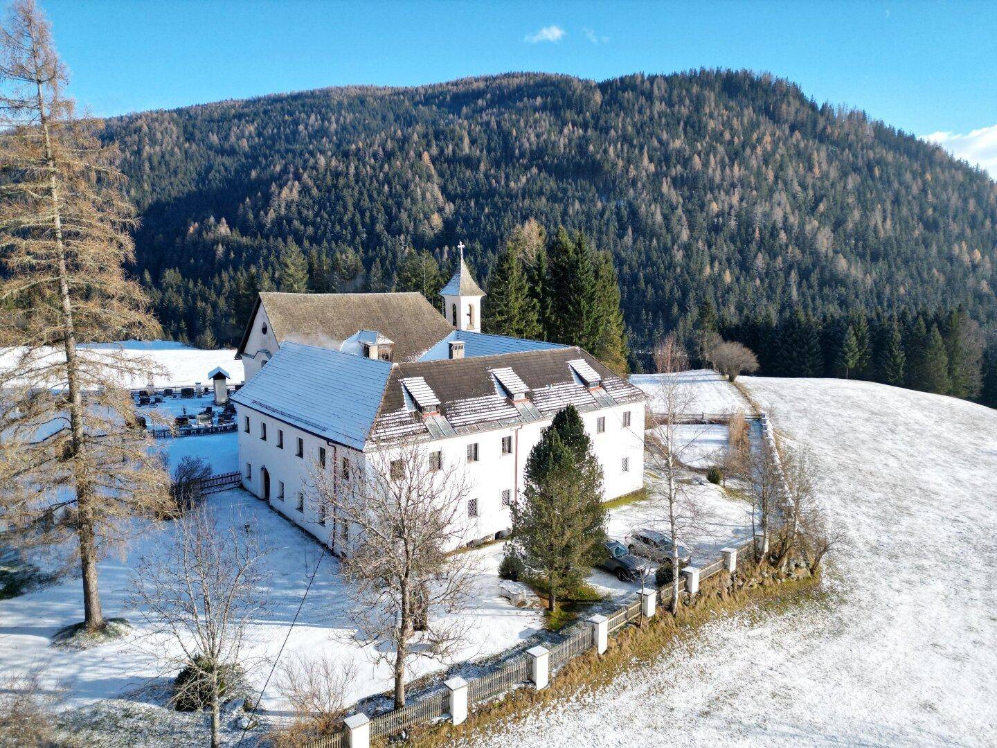 Historisches Gebäude in einer weiten, verschneiten Landschaft mit Waldhügeln im Hintergrund.