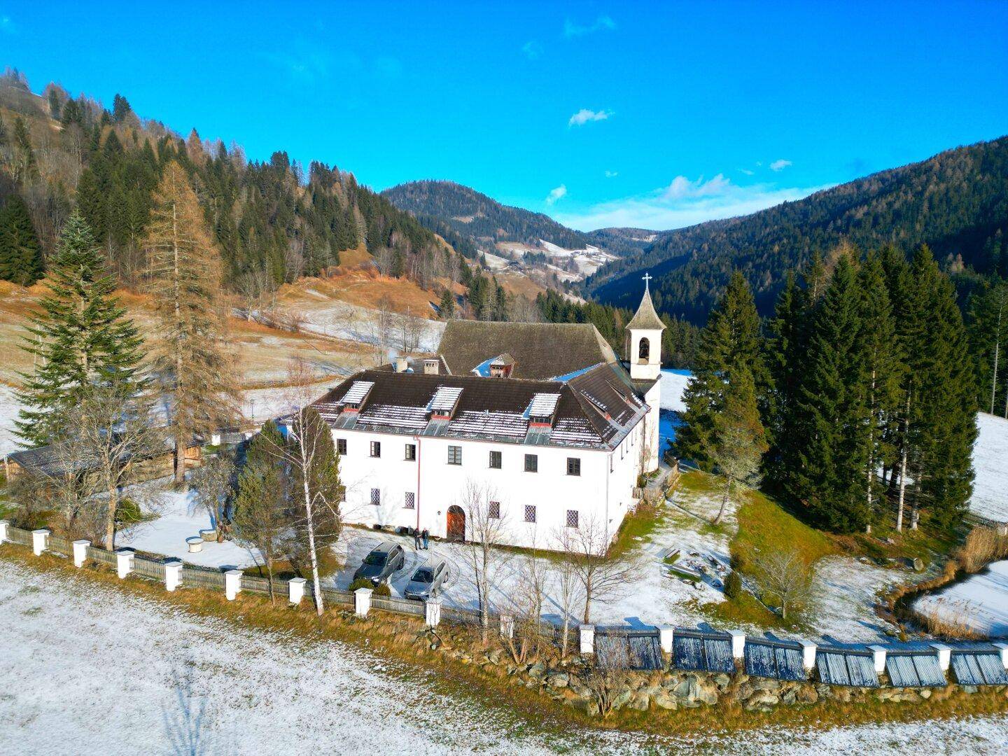Historisches Anwesen in verschneiter Berglandschaft mit umliegenden Wäldern und klarem Himmel.