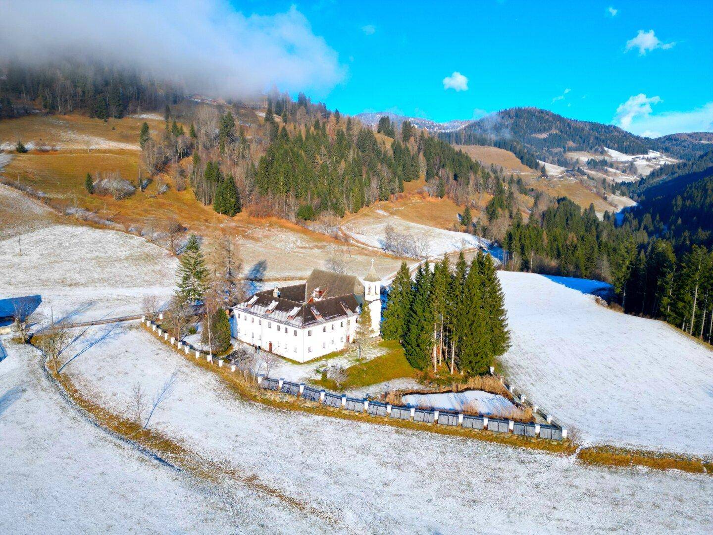 Weitläufiges Anwesen in verschneiter Berglandschaft mit Wald und klarem blauen Himmel.