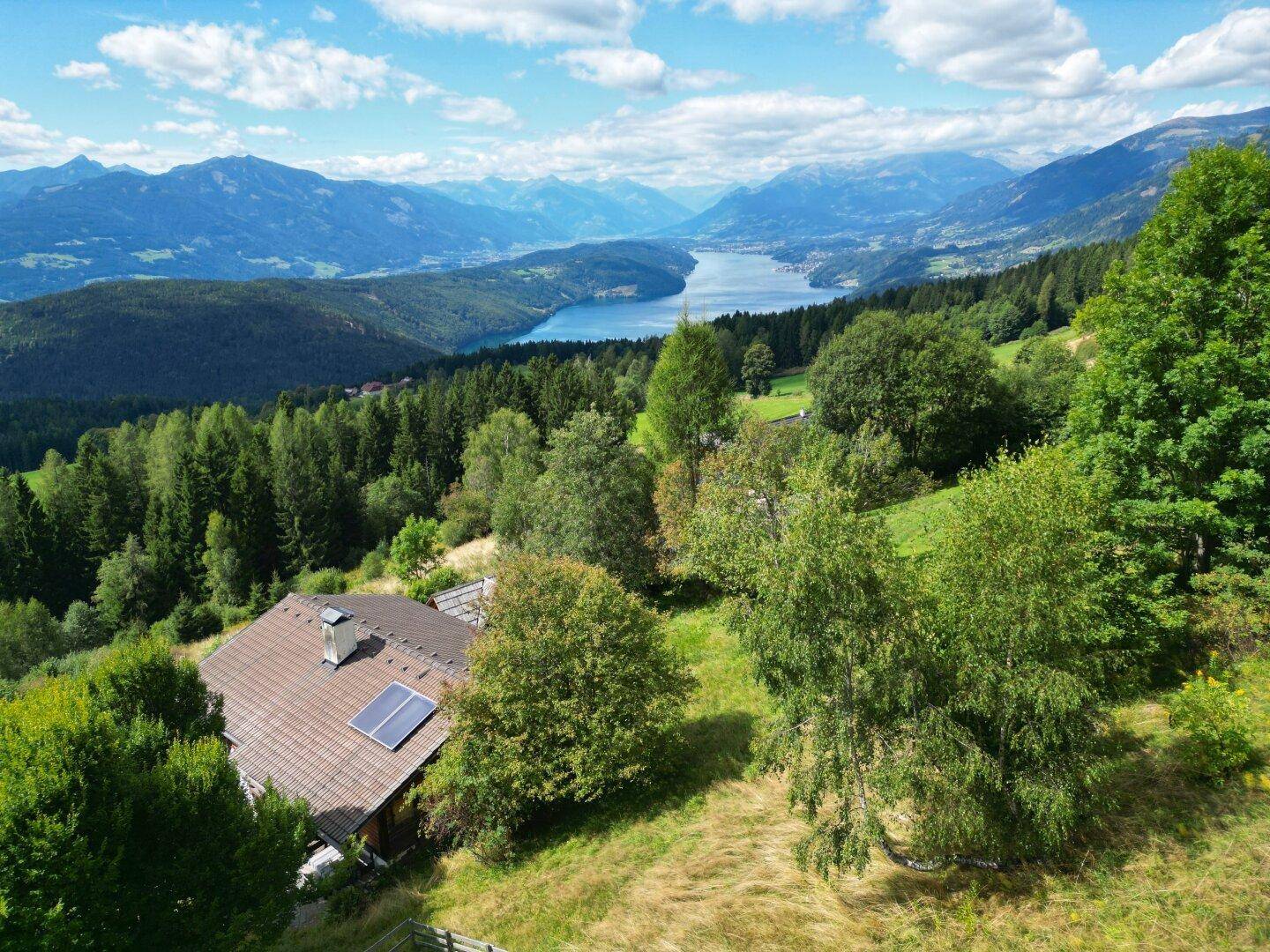 Panoramablick auf ein Haus mit Solaranlage, umgeben von grünen Hügeln und einem See in der Ferne.