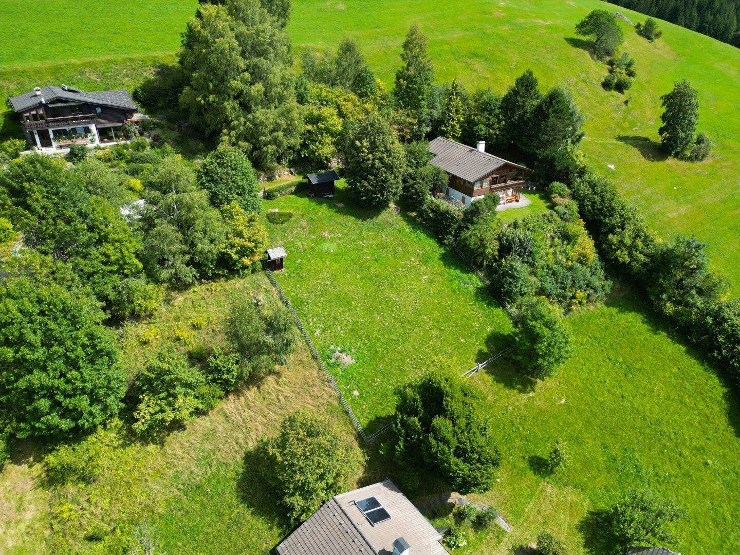 Luftaufnahme eines weitläufigen Grundstücks mit mehreren Häusern und viel Grünfläche in den Bergen.