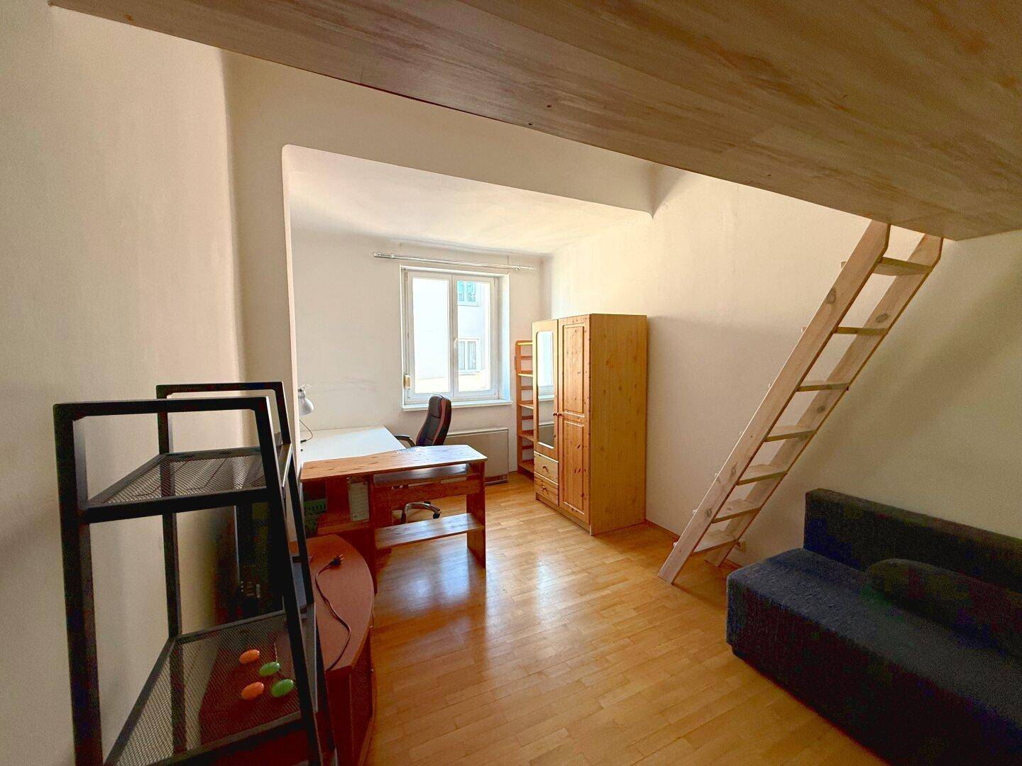 Multifunktionaler Raum mit Schreibtisch, Holzschrank und Leiter zu einem Hochbett.