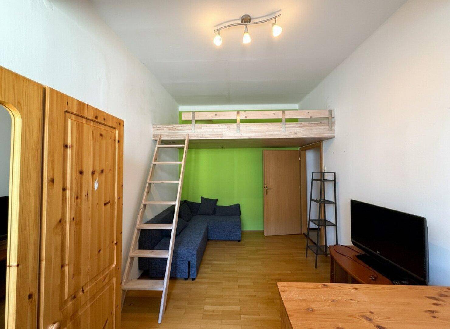 Wohnbereich mit Hochbett, Sofa und Fernseher, ideal für kompaktes Wohnen.