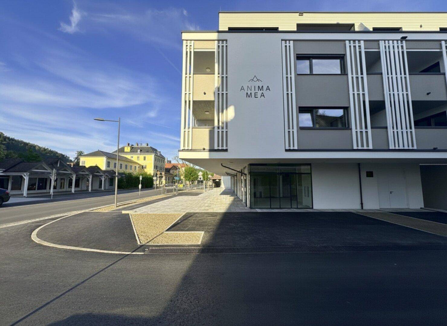 Eckansicht eines modernen Neubaus mit weißer und grauer Fassade, großen Fenstern und dem Schriftzug "ANIMA MEA" an der Wand.