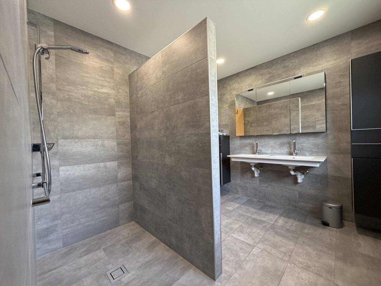 Modernes Badezimmer mit grauen Fliesen, einer begehbaren Dusche und einem Doppelwaschbecken.