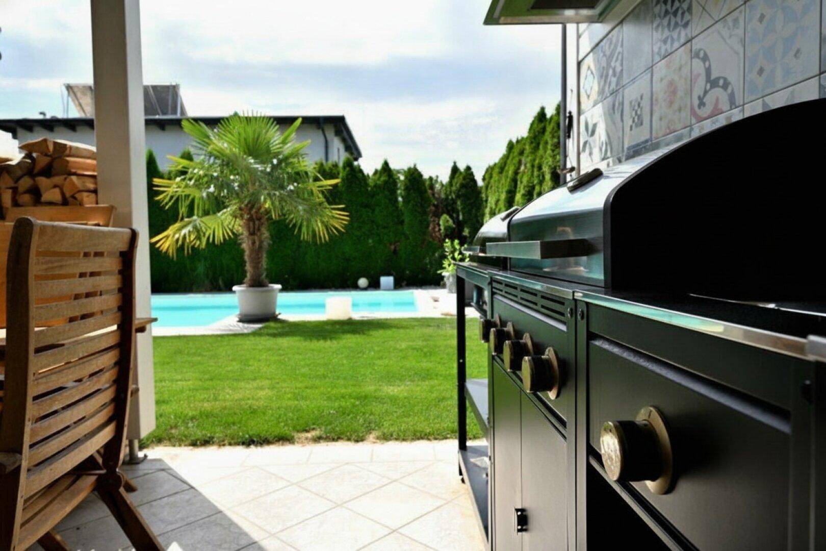 Moderner Grillbereich im Freien mit großem Grill und Blick auf den Pool und Garten.
