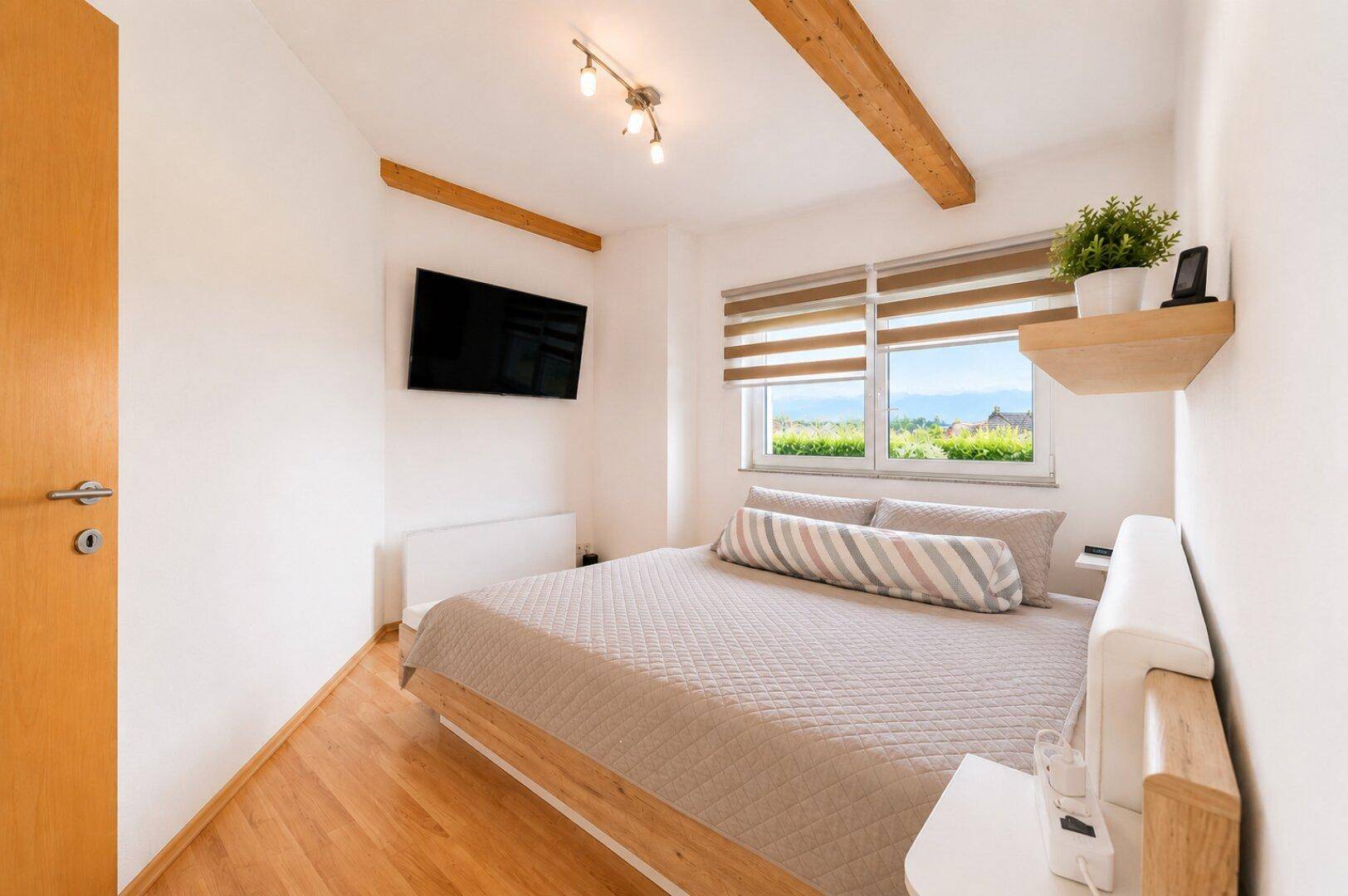 Gemütliches Schlafzimmer mit Holzboden, sichtbaren Holzbalken und schöner Aussicht.