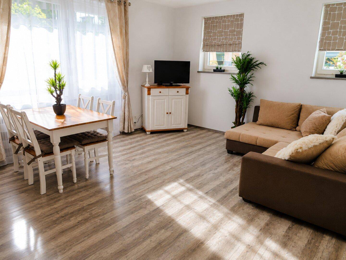 Helles Wohn-Esszimmer mit Laminatboden, beigem Ecksofa und einem Esstisch am Fenster.