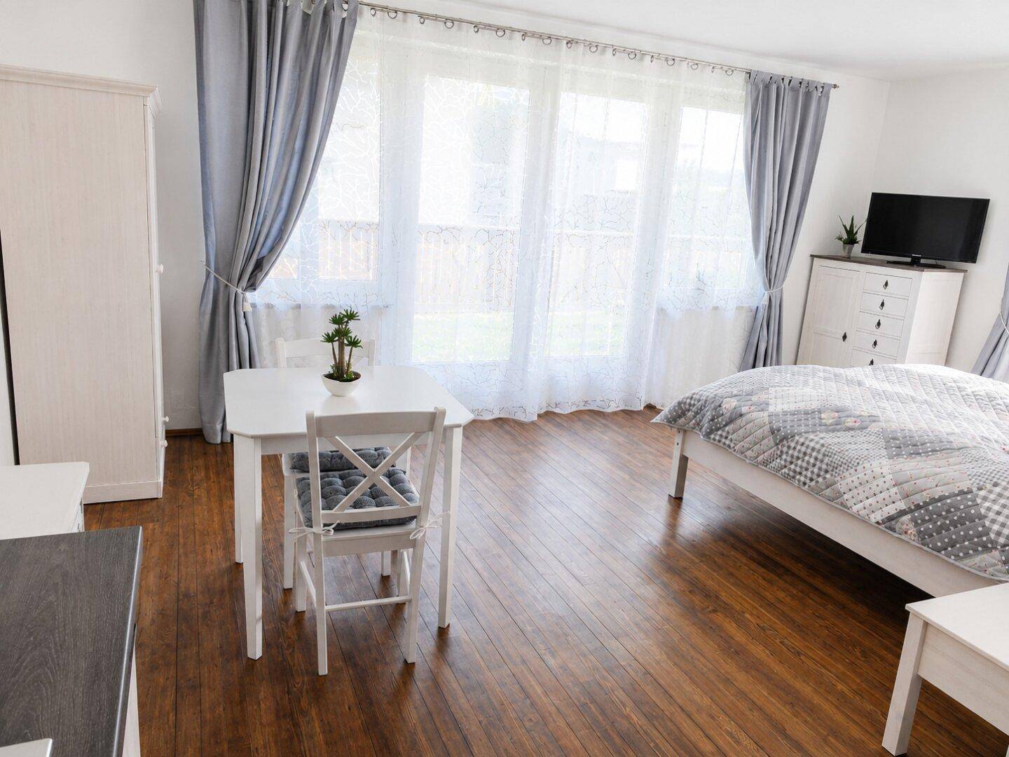 Helles Schlafzimmer mit Holzboden, großem Fenster und einem Esstisch für zwei Personen.