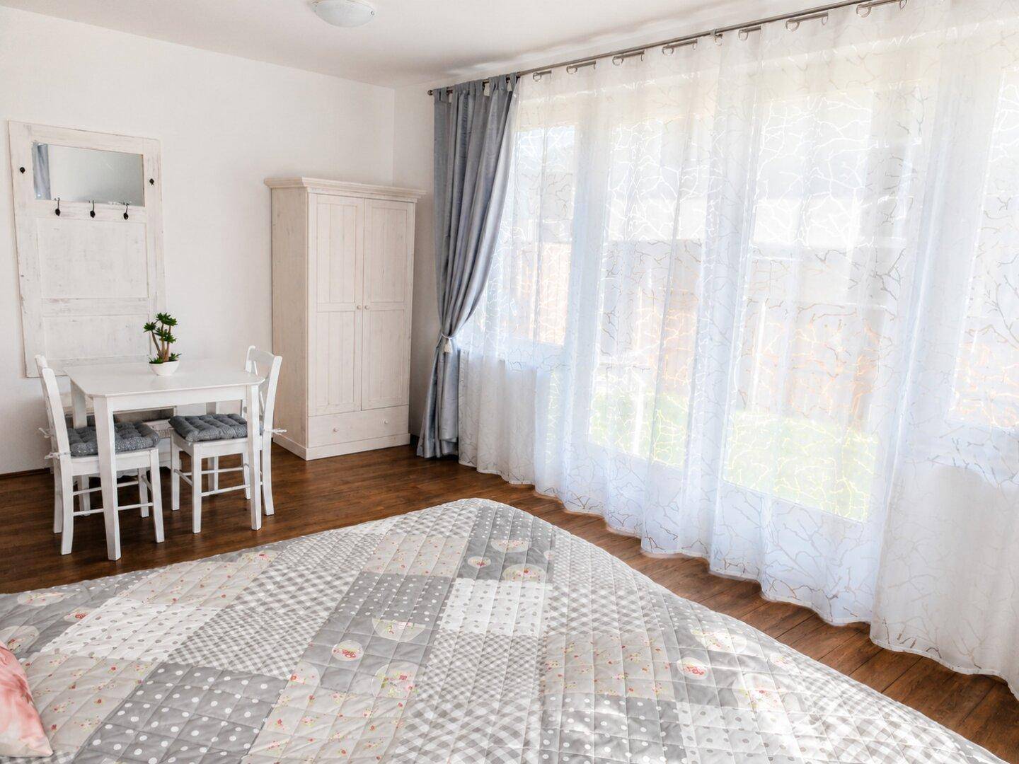 Geräumiges Schlafzimmer mit Holzboden, großem Bett und viel Tageslicht durch die breite Fensterfront.