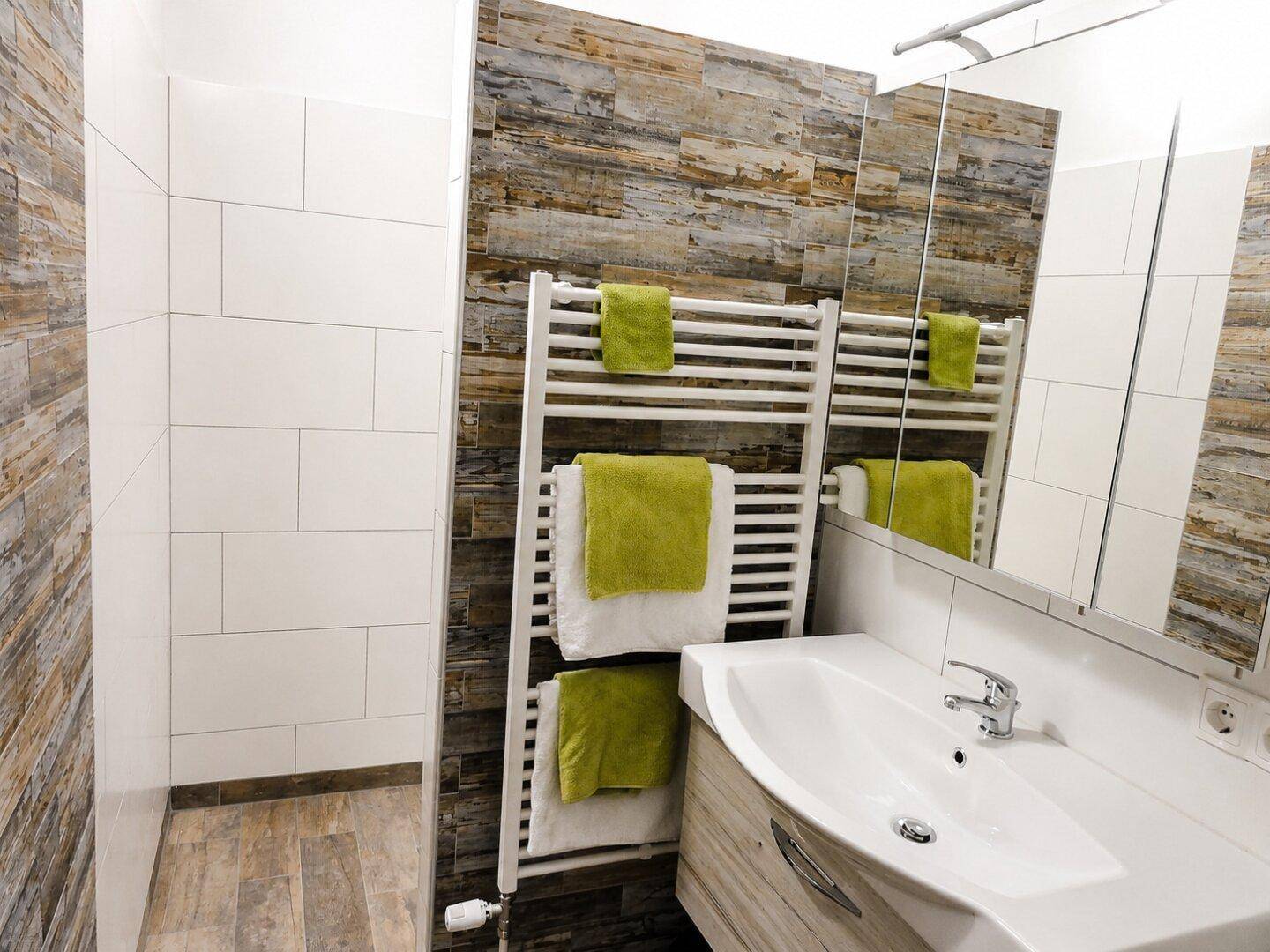 Modernes Badezimmer mit Holzoptik-Fliesen, weißem Waschbecken und beheiztem Handtuchhalter.