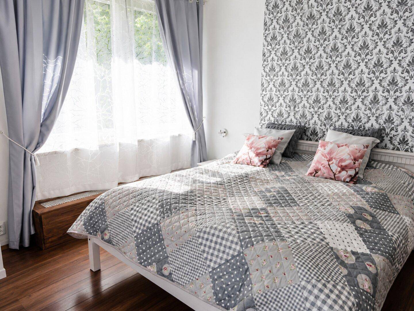 Gemütliches Schlafzimmer mit großem Bett, gemusterter Tapete und viel natürlichem Licht.