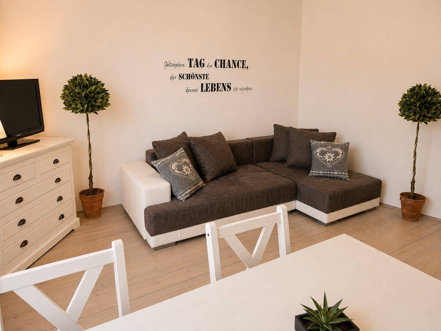 Heller Wohnbereich mit großem Ecksofa, Holzboden und dekorativen Pflanzen.