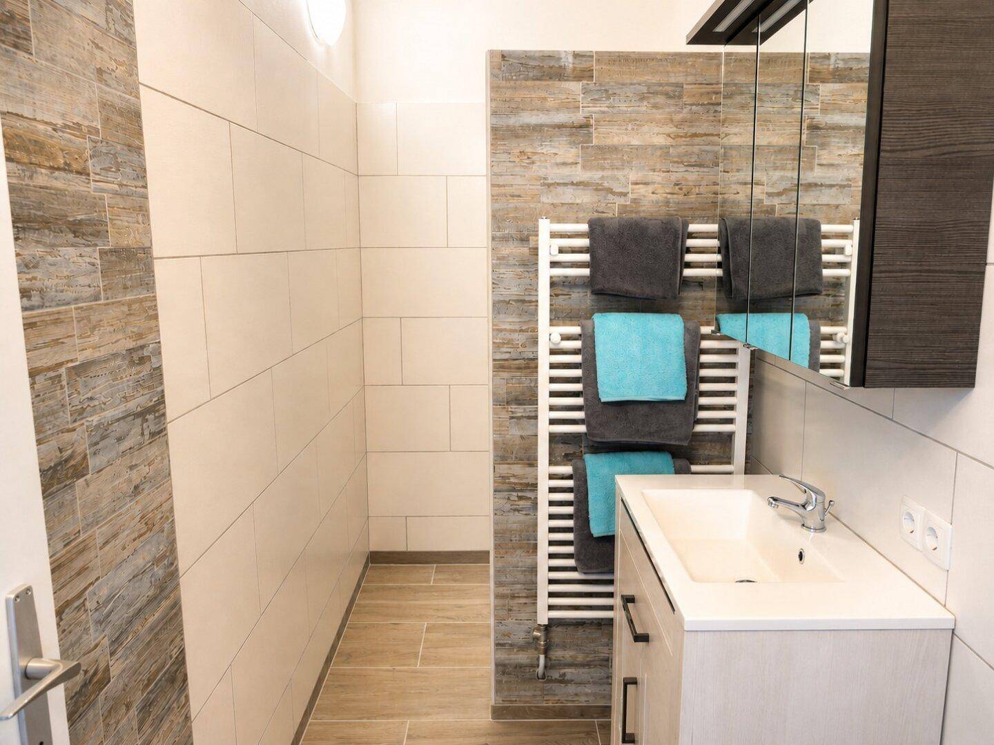 Modernes Badezimmer mit Holzoptik-Fliesen, weißem Waschbecken und beheiztem Handtuchhalter.