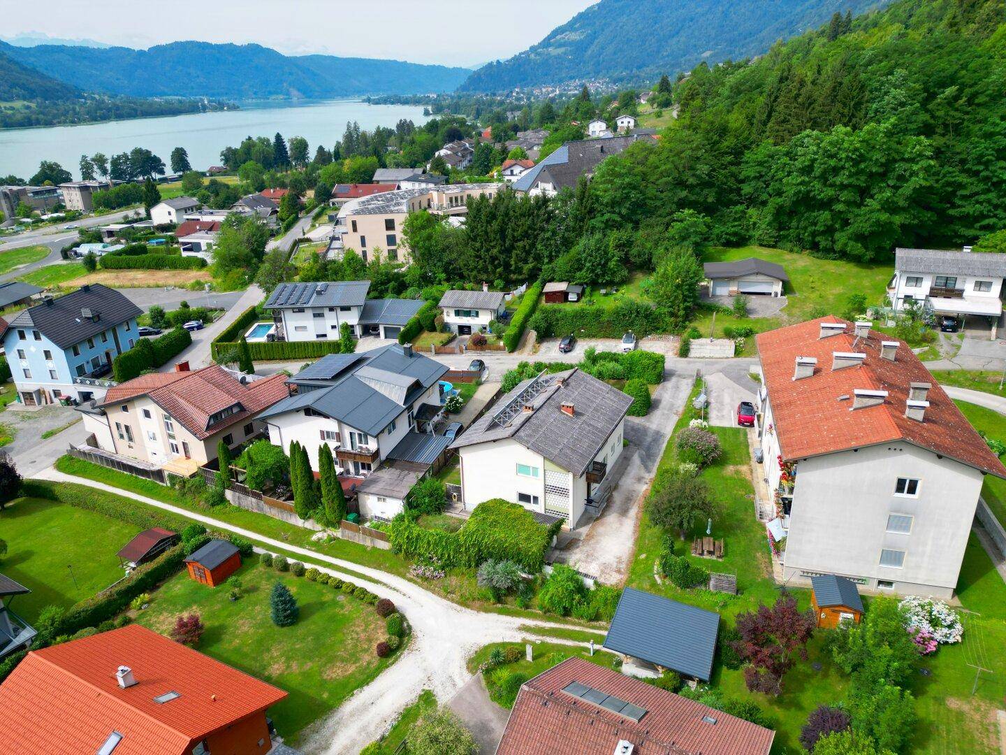 Weitläufige Luftaufnahme einer Wohnsiedlung mit See- und Bergblick, umgeben von üppiger Natur.