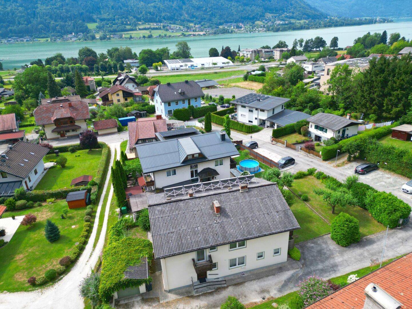 Luftaufnahme einer Wohnsiedlung mit See- und Bergblick, umgeben von üppiger Natur und vielen Bäumen.