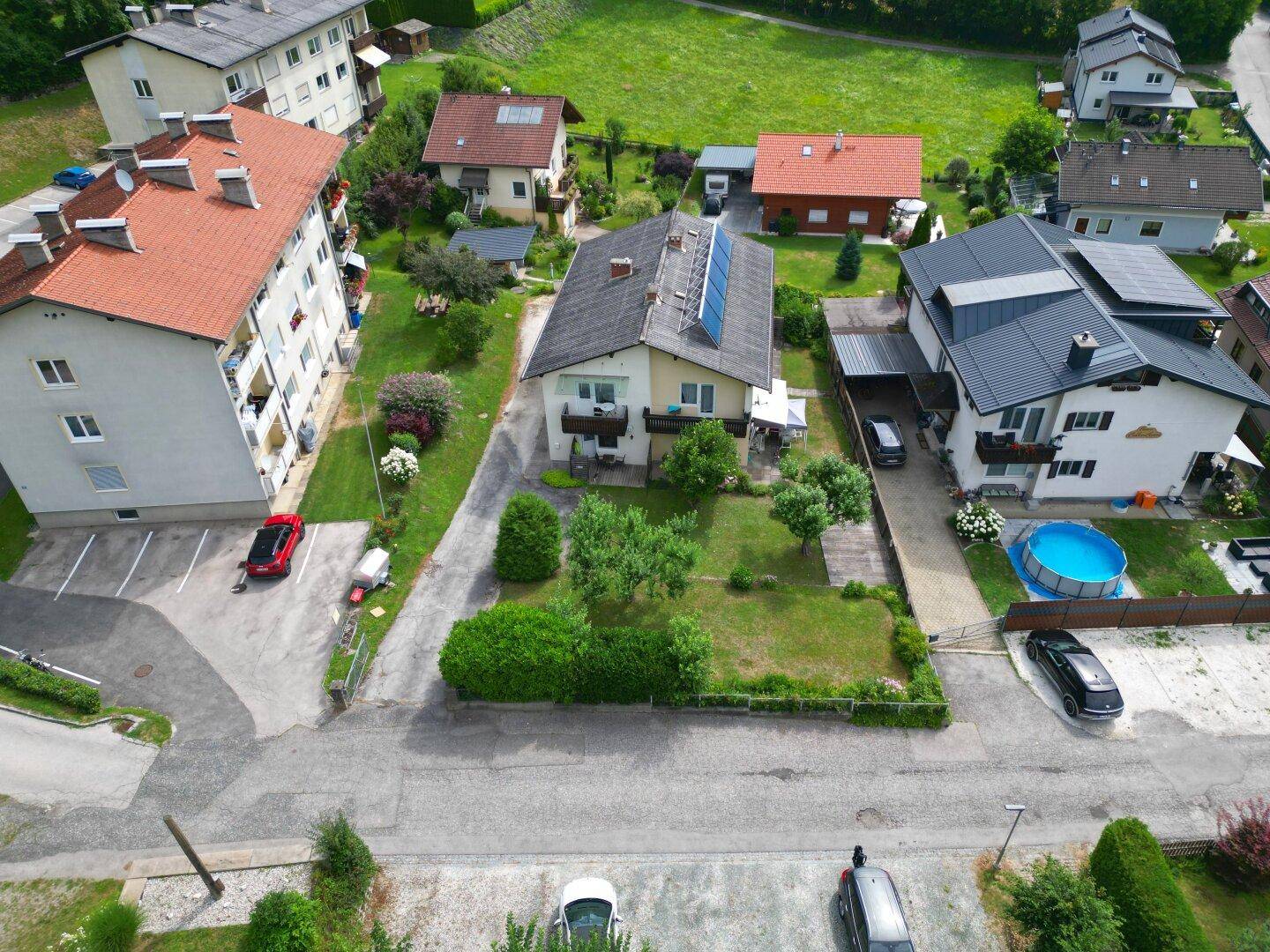 Vogelperspektive eines Wohnhauses mit Garten und Photovoltaikanlage, umgeben von Nachbarhäusern und Grünflächen.