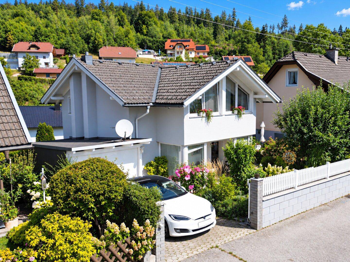 Nahaufnahme des Einfamilienhauses mit weißer Fassade, gepflegtem Vorgarten und einem modernen Auto in der Einfahrt.