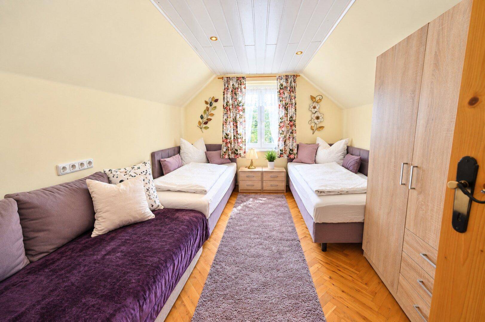 Helles Schlafzimmer mit zwei Einzelbetten, einem Sofa und schrägen Decken, farbenfroh eingerichtet.