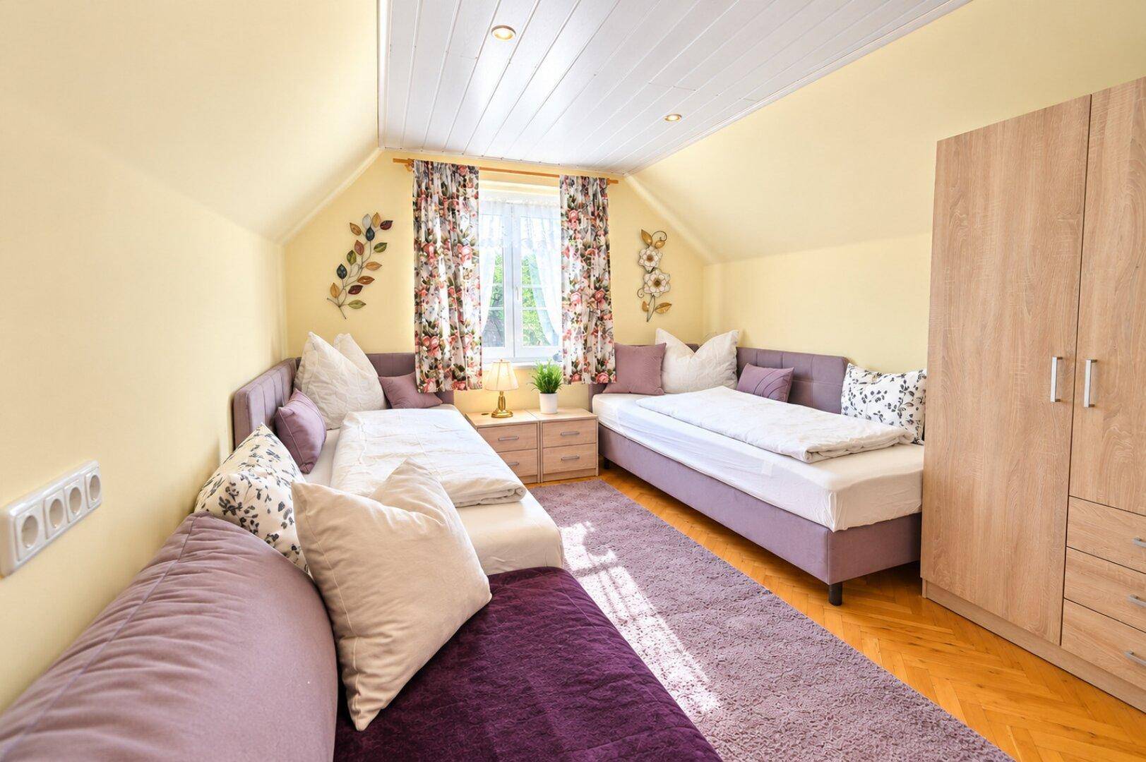 Gemütliches Schlafzimmer mit zwei Einzelbetten, einem Sofa und schrägen Decken, mit floralen Vorhängen.