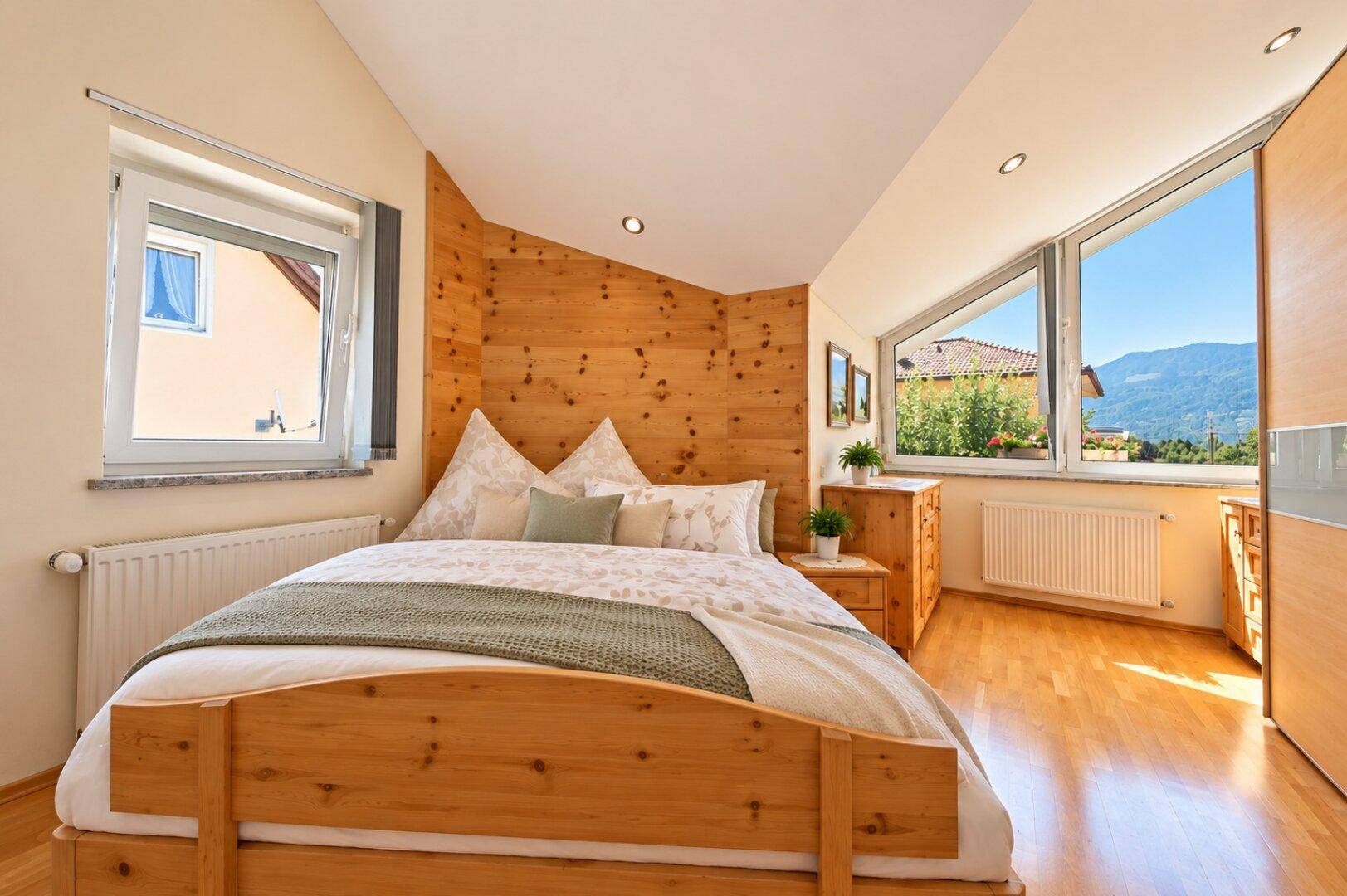 Gemütliches Schlafzimmer mit Holzbett, Holzwandverkleidung und großen Fenstern mit Bergblick.