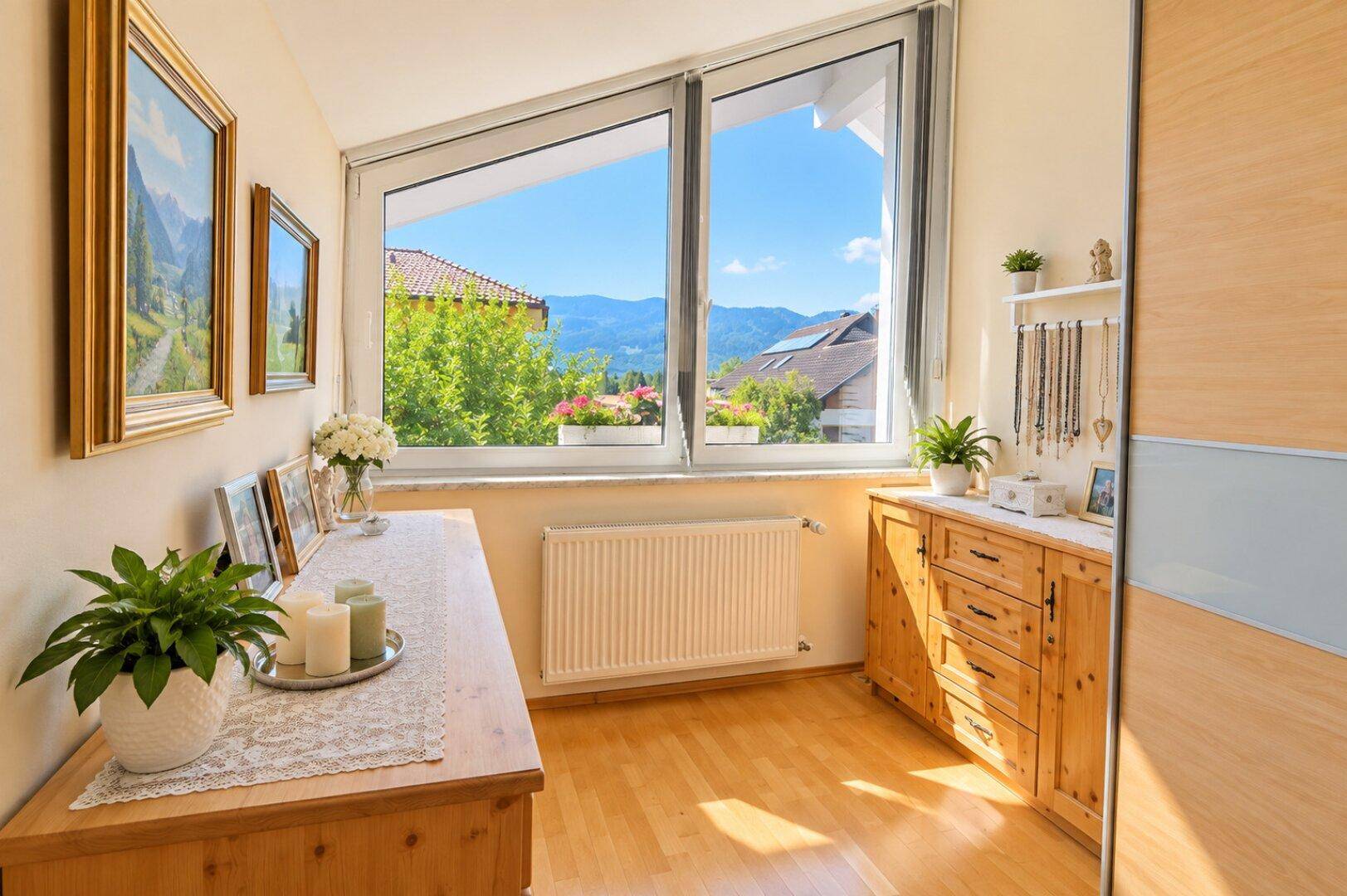 Heller Raum mit Holzboden, Kommoden und großen Fenstern, die einen weiten Blick auf die Berge bieten.