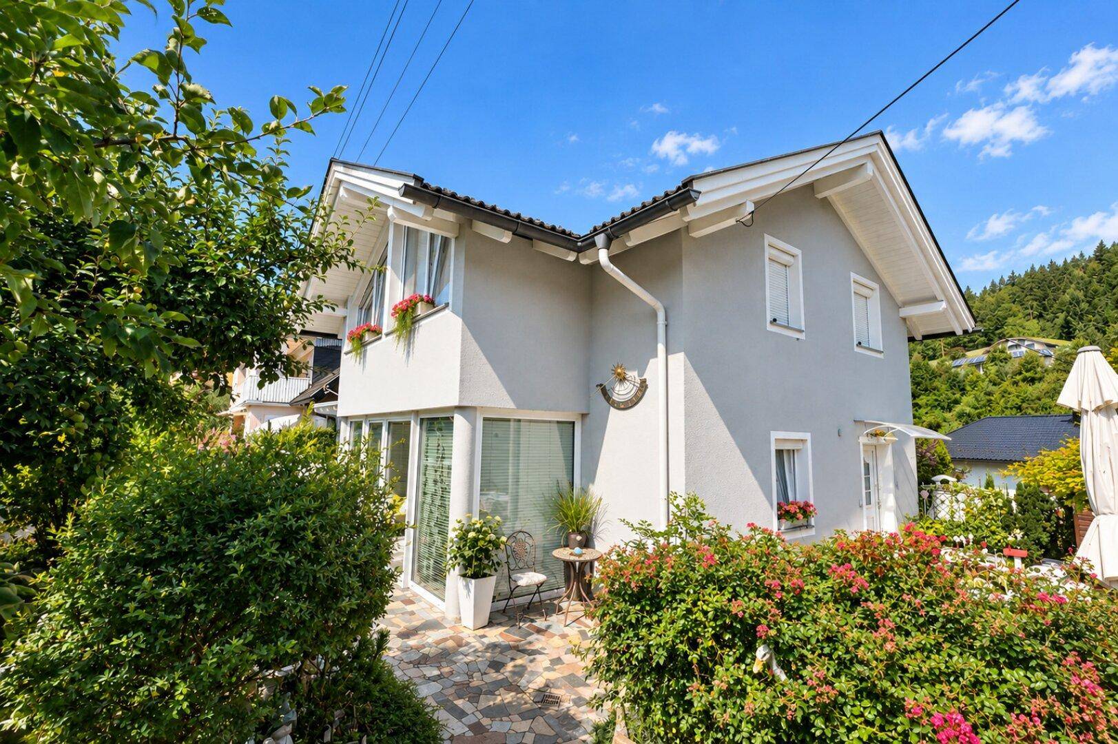 Das Einfamilienhaus von der Gartenseite, mit einer kleinen Terrasse und blühenden Sträuchern.