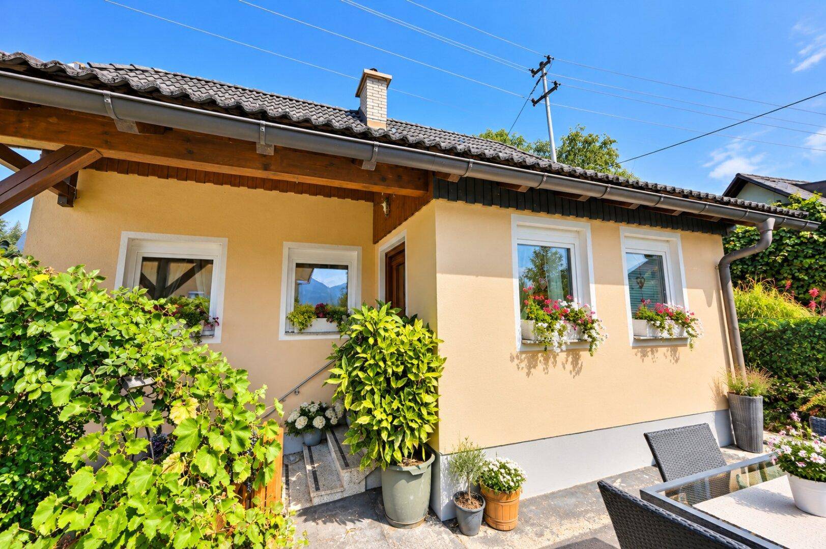 Seitliche Ansicht des Hauses mit einer kleinen Terrasse und üppiger Vegetation im Vorgarten.