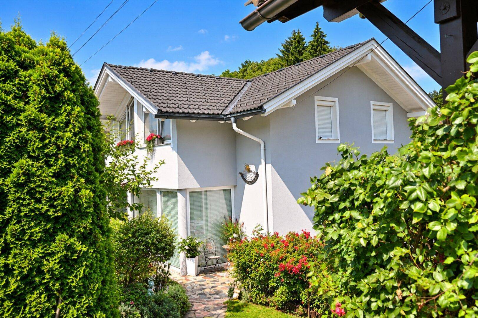 Ansicht des Hauses von der Gartenseite, umgeben von üppigem Grün und hohen Hecken.