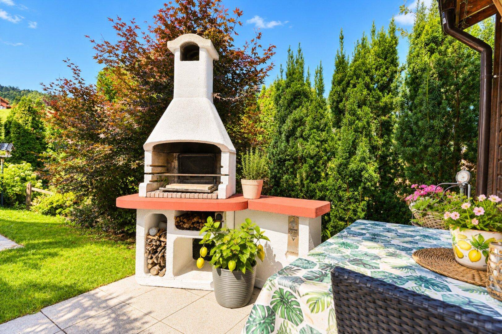 Gepflegter Gartenbereich mit einem gemauerten Grillplatz und einem Esstisch im Freien.