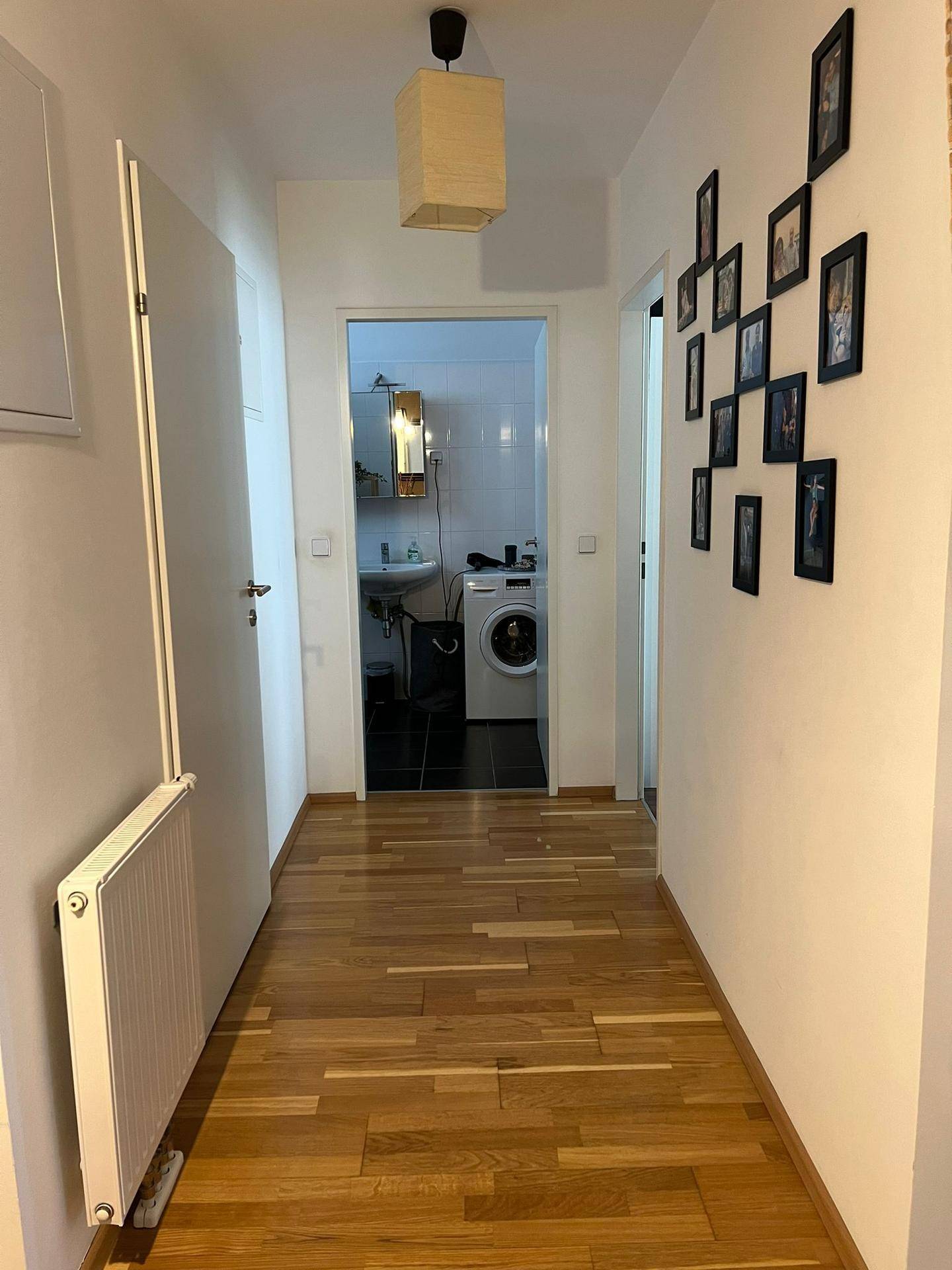 Heller Flur mit Holzboden, Heizkörper und Zugang zu einem Badezimmer mit Waschmaschine.