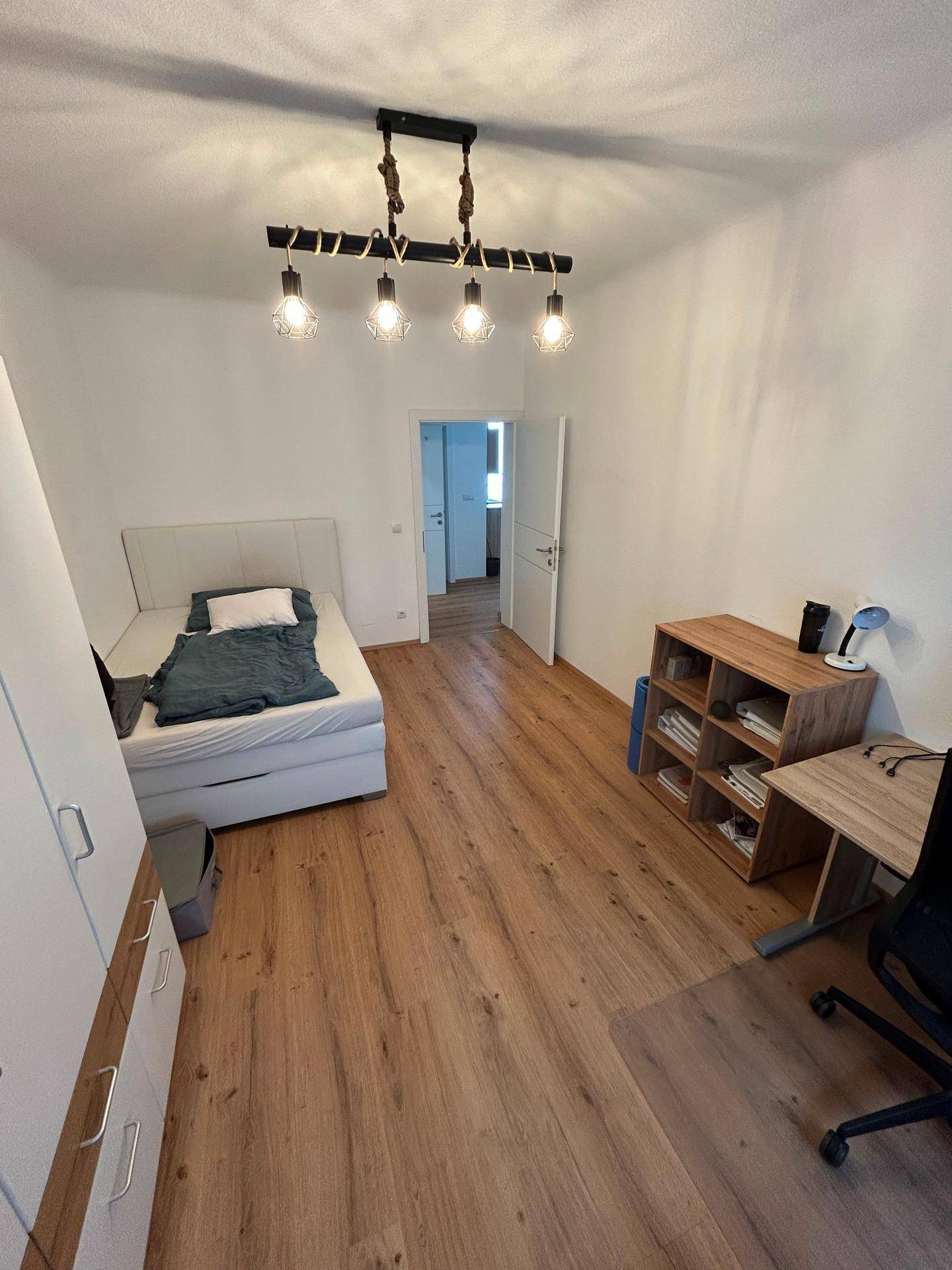 Geräumiges Schlafzimmer mit Bett, Schreibtisch und Kleiderschrank, mit Holzboden.