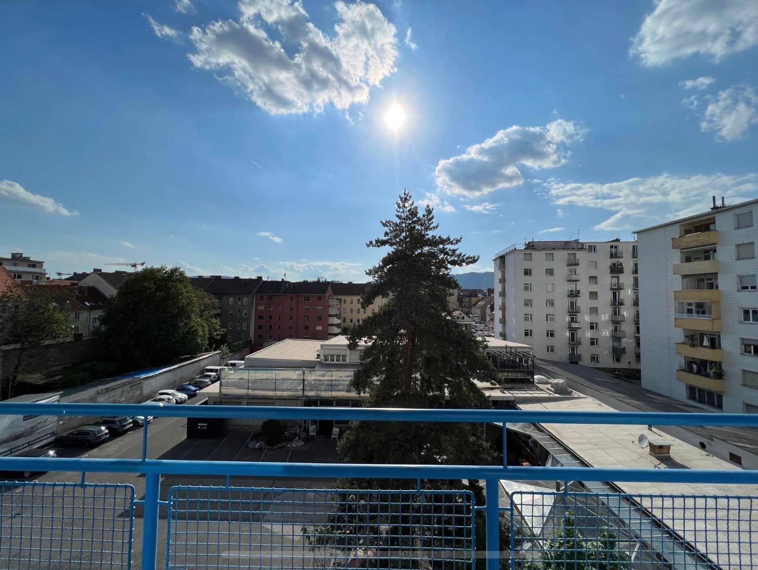 Sonniger Ausblick vom Balkon auf umliegende Gebäude und einen klaren blauen Himmel.