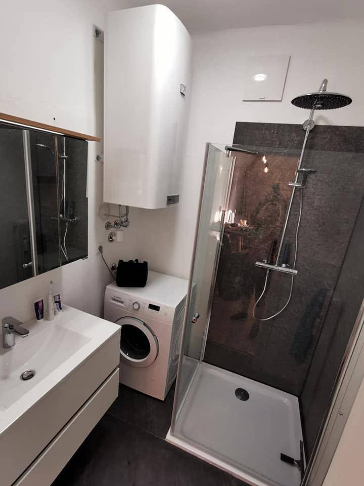 Modernes Badezimmer mit Dusche, Waschbecken und Waschmaschine, in hellen und dunklen Tönen.